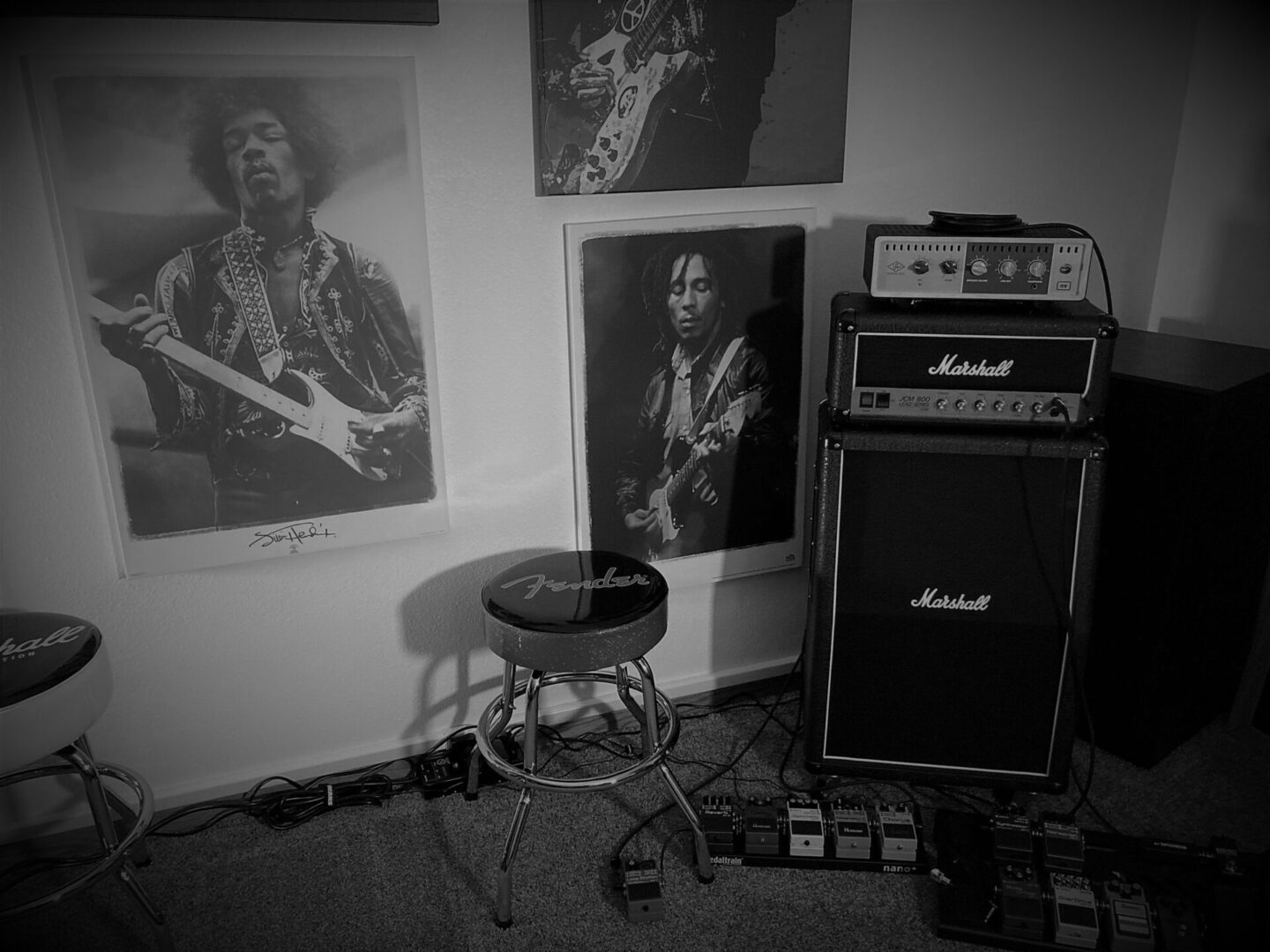 wall of posters of famous guitarists next to amps